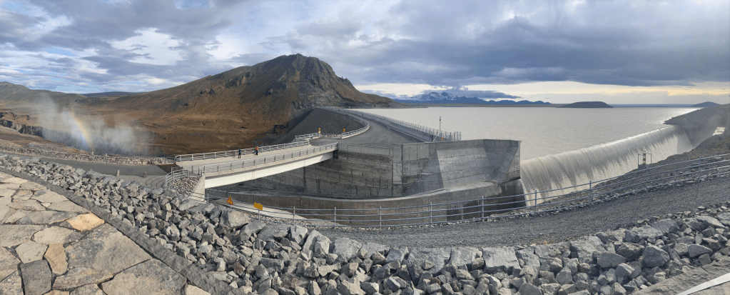 A panorama photo of a dam with sea and mountains in the background